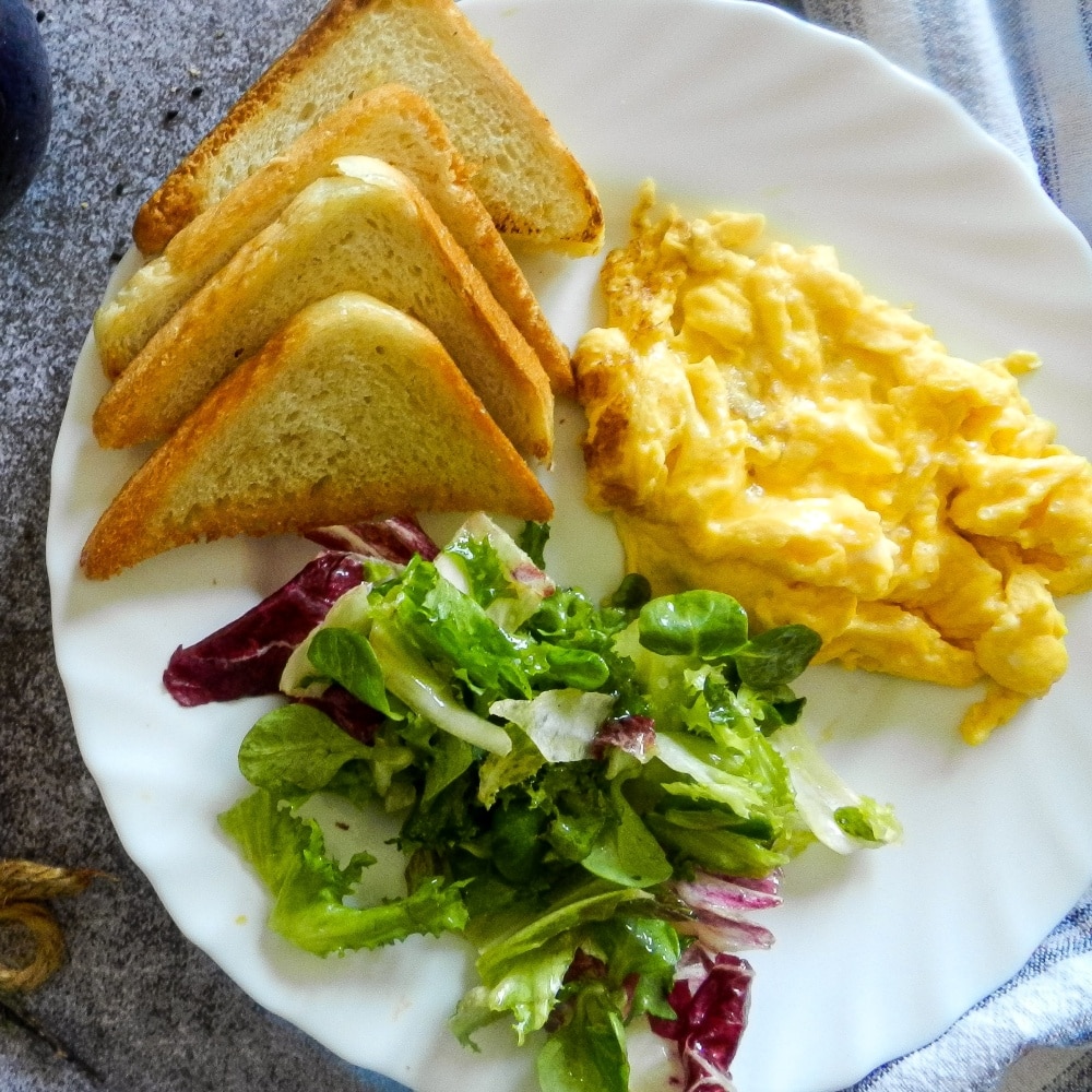 Soft scrambled egg, toast, and salad on plate